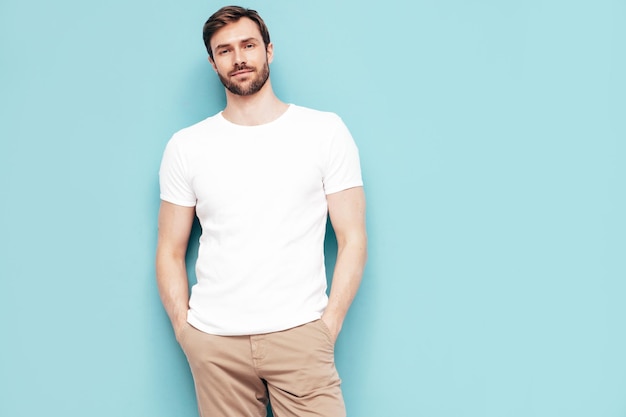 Portret van knappe lachende stijlvolle hipster lamberseksueel model Sexy man gekleed in T-shirt en broek Mode man geïsoleerd op blauwe muur in studio