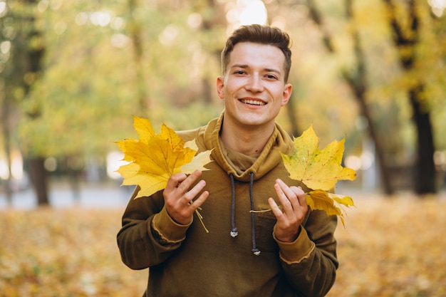 Portret van knappe man glimlachend en met een boeket van herfstbladeren in het park