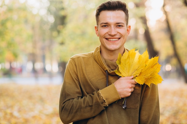 Portret van knappe man glimlachend en met een boeket van herfstbladeren in het park