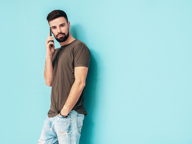 Portret van knappe zelfverzekerde stijlvolle hipster lamberseksueel model man gekleed in tshirt en jeans mode man geïsoleerd op blauwe muur in studio