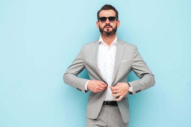 Portret van knappe zelfverzekerde stijlvolle hipster lamberseksueel model moderne man gekleed in elegante pak mode man poseren in studio in de buurt van blauwe muur in zonnebril
