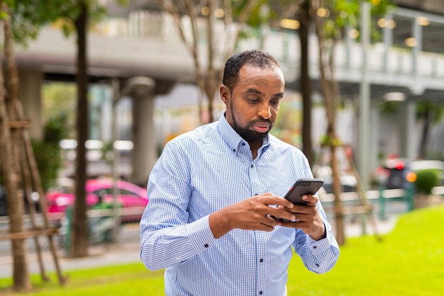 Portret van knappe zwarte man in de stad met behulp van telefoon