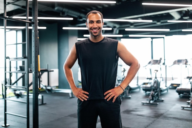 Portret van knappe zwarte Personal Trainer poseren In Fitness Club interieur