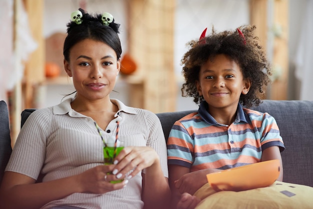 Portret van lachende afro-amerikaanse familie in halloween-kostuums zittend op de bank in de woonkamer