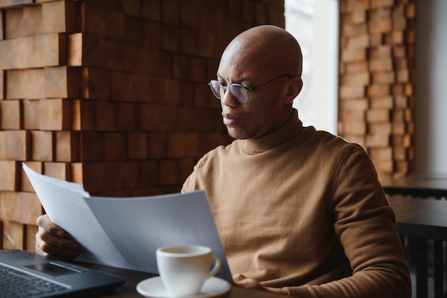 Portret van lachende Afro-Amerikaanse man met bril zit aan bureau in kantoor werken op laptop, gelukkige biraciale mannelijke werknemer kijkt naar camera poseren, druk bezig met het gebruik van moderne computergadget op werkplek