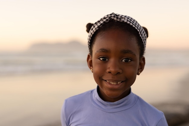 Portret van lachende Afro-Amerikaanse schattig meisje hoofdband dragen tegen zee en heldere hemel bij zonsondergang