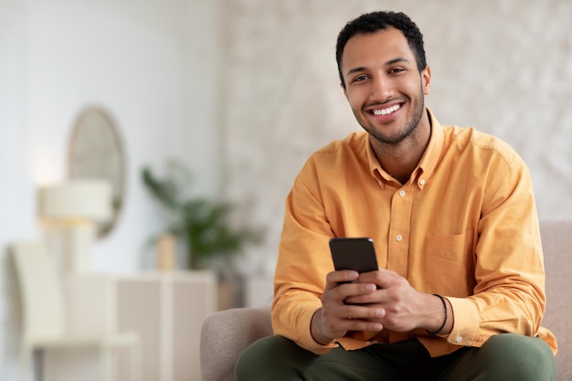 Portret van lachende Arabische man met smartphone thuis poseren