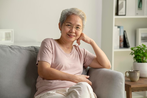 Portret van lachende aziatische senior vrouw zittend op de bank thuis