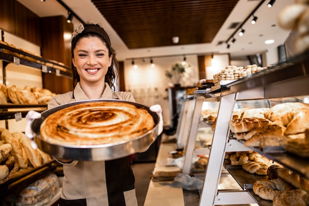 Portret van lachende bakkerijmedewerker met versgebakken taart in bakkerijwinkel