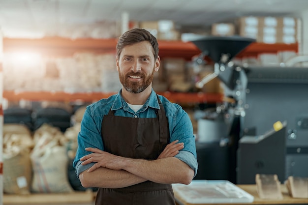 Portret van lachende bedrijfseigenaar op de achtergrond van een eigen kleine koffiefabriek