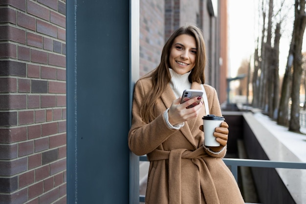 Portret van lachende brunette vrouw met kopje koffie en smartphone