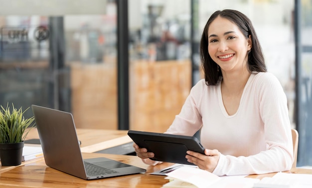 Portret van lachende dame ondernemer bezig met laptop en tablet op de werkplek in loft kantoor Kijkend naar de camera