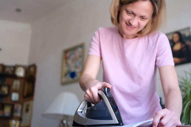 Portret van lachende gelukkige vrouw strijkt kleren op strijkplank vrouwelijke huisvrouw die huishoudelijk werk doet