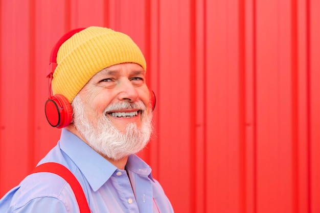 Portret van lachende gepensioneerde man luisteren naar muziek met koptelefoon geïsoleerd op rode achtergrond