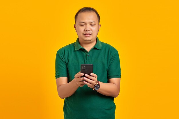 Portret van lachende jonge Aziatische man met behulp van een mobiele telefoon op gele achtergrond