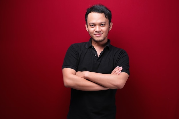 Portret van lachende jonge Aziatische man met zwart shirt geïsoleerd op rood