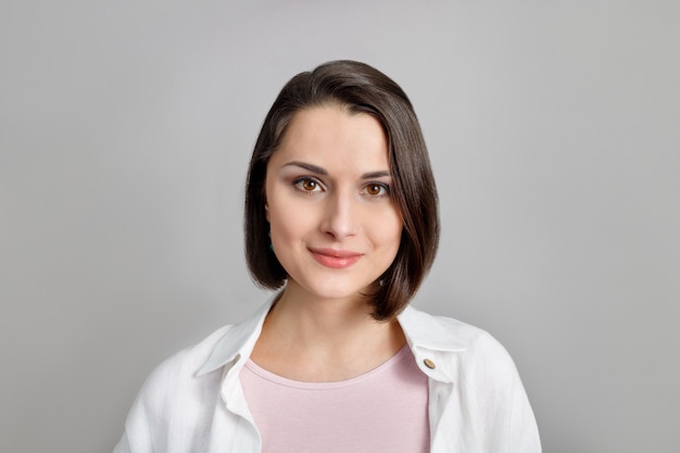 portret van lachende jonge brunette multi-etnische vrouw in roze tank en wit overhemd kijk naar de camera