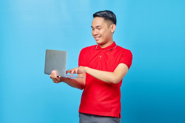 Portret van lachende jonge knappe man die een laptop vasthoudt en gebruikt op blauwe achtergrond