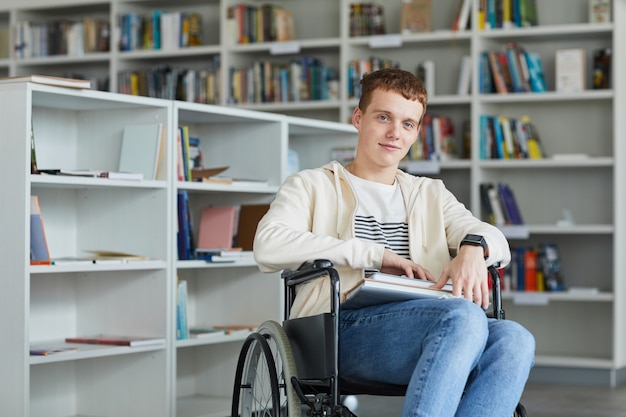 Portret van lachende jonge man met rolstoel in schoolbibliotheek en,