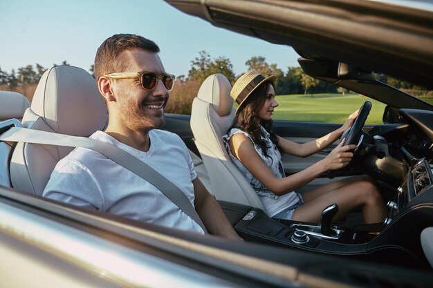 Portret van lachende jonge man met vriendin cabriolet rijden op de landweg