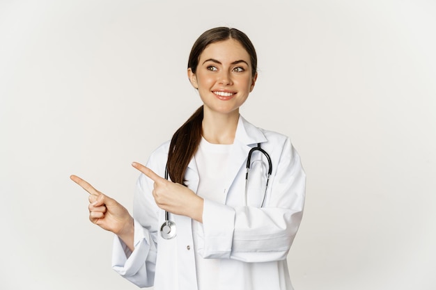 Foto portret van lachende jonge vrouw arts gezondheidszorg medisch werker wijzende vingers links tonen kliniek...