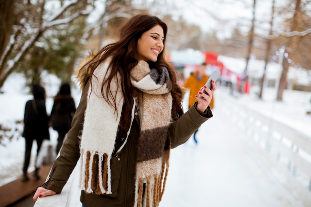 Portret van lachende jonge vrouw met mobiele telefoon in de winter buiten