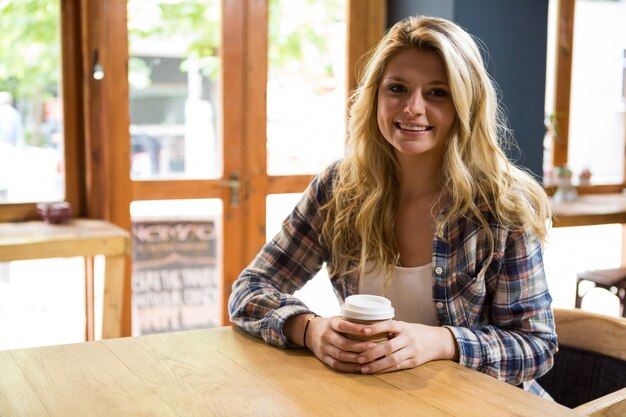 Portret van lachende jonge vrouw met wegwerp koffiekopje in café