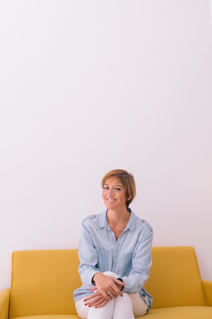 Portret van lachende jonge vrouw op gele bank