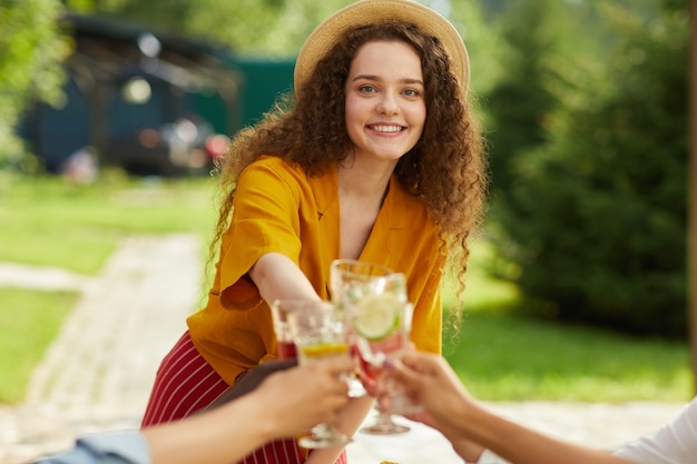 Portret van lachende jonge vrouw roosteren met vrienden terwijl u geniet van diner op terras in de zomer