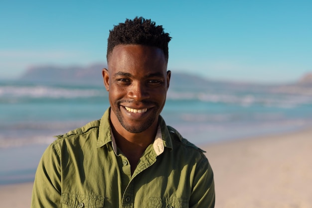 Portret van lachende knappe Afro-Amerikaanse jongeman tegen zee en blauwe lucht tijdens zonsondergang