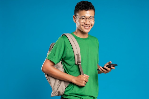 Portret van lachende knappe jonge man met smartphone, geïsoleerd op blauwe achtergrond