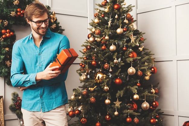 Portret van lachende knappe man met cadeau. Sexy bebaarde man poseren in de buurt van kerstboom met heden.