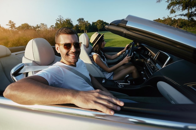 Portret van lachende man met vriendin die overdag in luxe cabrio rijdt