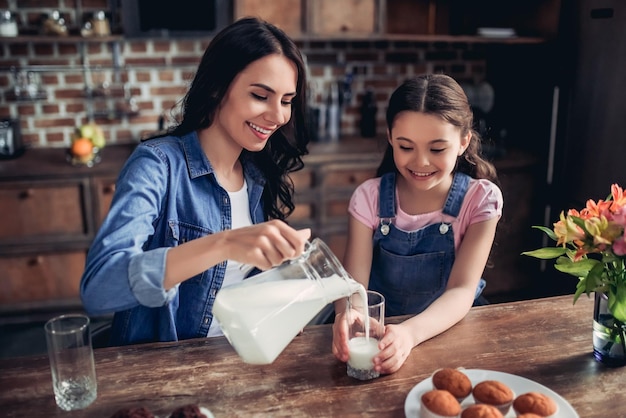 Portret van lachende moeder die melk in het glas giet voor dochter in de keuken