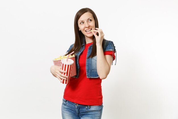 Portret van lachende mooie vrouw kijken naar film, popcorn eten uit emmer, plastic beker frisdrank of cola vasthouden, opzij kijkend op kopieerruimte geïsoleerd op een witte achtergrond. Emoties in de bioscoop.