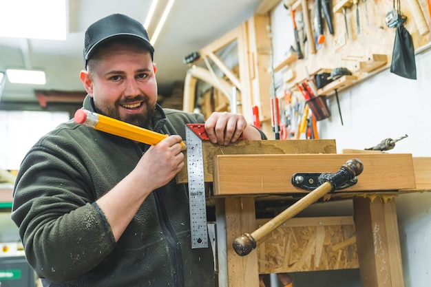 Foto portret van lachende timmerman die een houten plank meet om te snijden met hoekliniaal en potlood