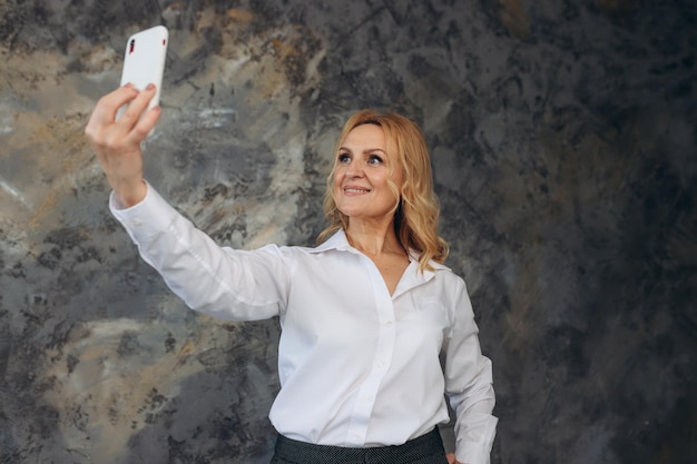 Portret van lachende volwassen vrouw selfie te nemen op telefoon geïsoleerd op gestructureerde achtergrond Succesvolle zakenvrouw Vrouw 50s