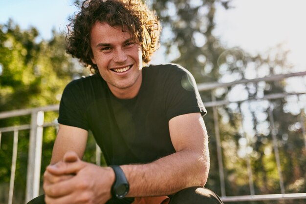 Portret van lachende vrolijke jonge man draagt zwarte tshirt en polshorloge op de straat van de stad Gelukkig man met krullend haar poseren voor advertentie met kopie ruimte buiten mensen concept