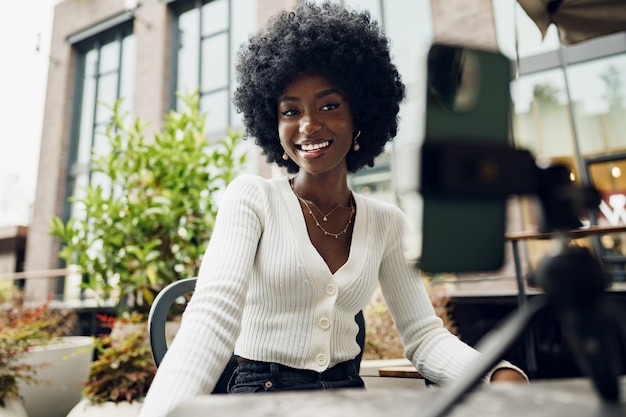 Portret van lachende vrouw met afro-kapsel op videogesprek zittend in café