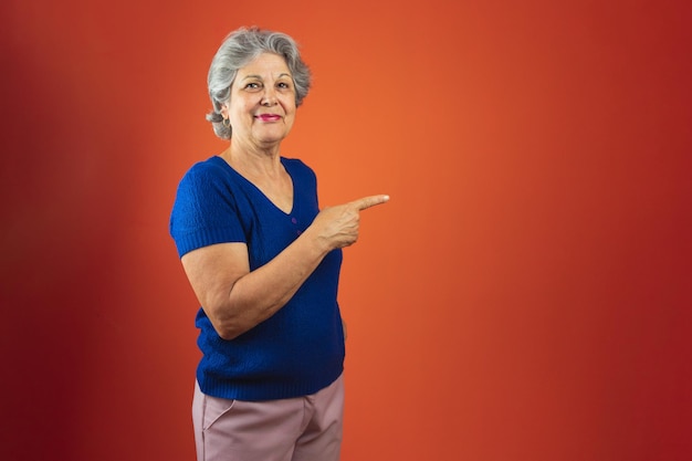 Portret van lachende vrouw met grijs haar en blauw T-shirt geïsoleerd over oranje achtergrond