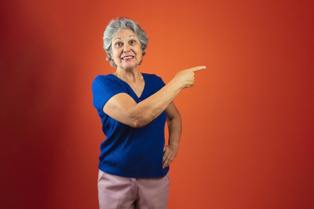 Portret van lachende vrouw met grijs haar en blauw T-shirt geïsoleerd over oranje achtergrond