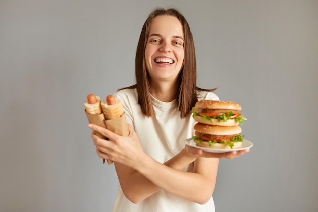 Portret van lachende vrouw met smakelijke cheeseburger en hotdogs gekruiste handen kijkend naar camera met vrolijke gelukkige uitdrukking houdt van ongezond voedsel