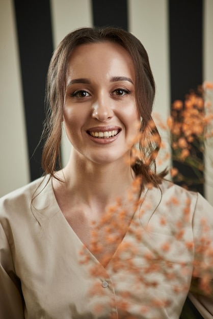 Portret van lachende vrouw schoonheidsspecialiste met bloemen Vrouwelijke schoonheidsspecialiste op haar werkplek in cosmetologie kliniek