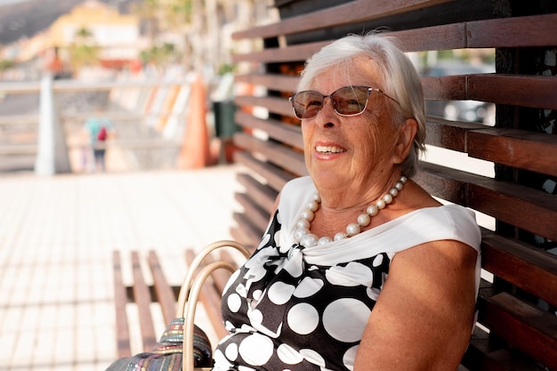 Portret van lachende whitehaired elegante senior vrouw zittend op bankje in park genieten van pensioen