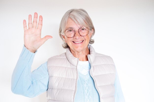 Foto portret van lachende whitehaired senior vrouw in bril zwaaiende hand op camera