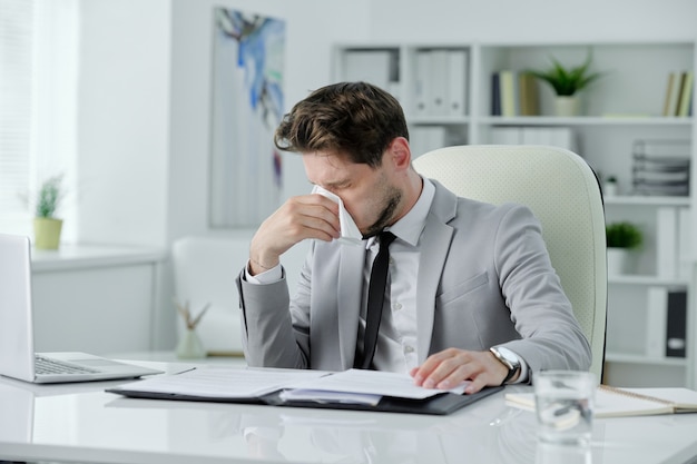 Portret van lachende zelfverzekerde jonge zakenman in zwarte stropdas die met gekruiste armen in de buurt van bureau in kantoor staat