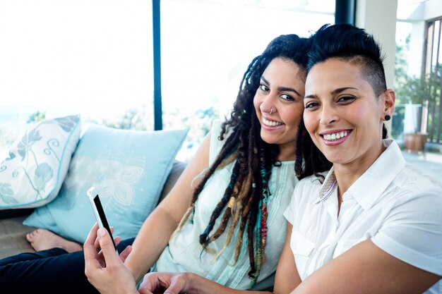 Portret van lesbische paarzitting op bank met mobiele telefoon in woonkamer