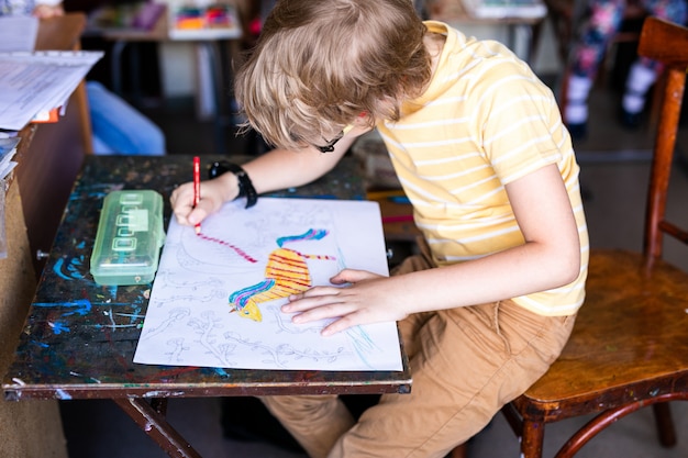 Portret van leuke jongen met schetspen en document bij bureau in klaslokaal