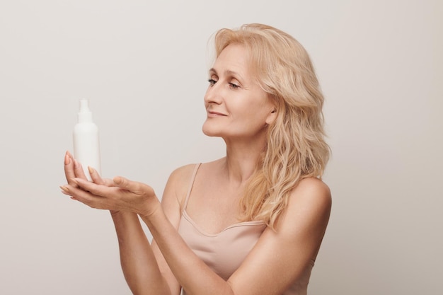 Portret van luxe jaren '50 volwassen blonde vrouw met cosmetisch product geïsoleerd op een witte achtergrond