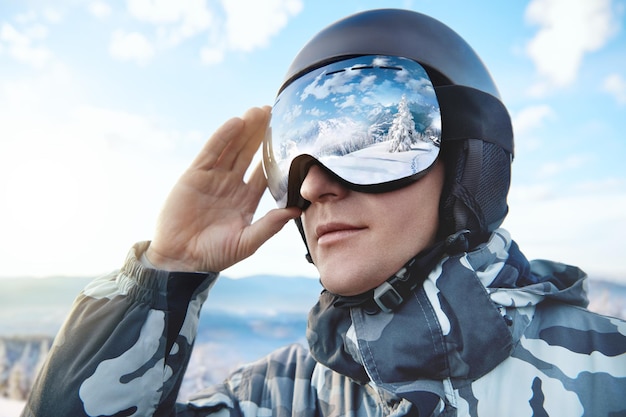 Portret van man op de achtergrond blauwe hemel houdt skibril met de weerspiegeling van besneeuwde bergen... Wintersport.